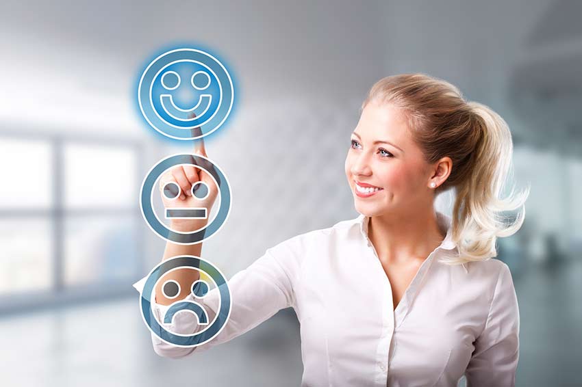 A smiling woman touching a smiley face icon on a touch screen